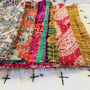 May include: A selection of patterned fabric pieces, possibly textiles or quilts, are arranged together. The fabrics feature floral, paisley, and striped designs in red, orange, green, and gold. White stitching is visible throughout the fabrics.