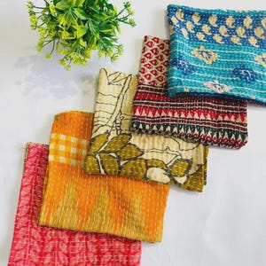 Puede incluir: Una colección de piezas de tela plegadas con varios patrones y diseños. Las telas presentan tonos de rojo, naranja, amarillo, verde y azul. Los patrones incluyen motivos florales, geométricos y abstractos. Una pequeña planta verde está en la esquina superior izquierda.