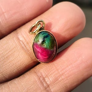 Peut inclure: Un pendentif en or avec une pierre précieuse ovale. La pierre précieuse présente un mélange de couleurs rouge, verte et foncée. Le pendentif est maintenu par une boucle en or pour une chaîne.