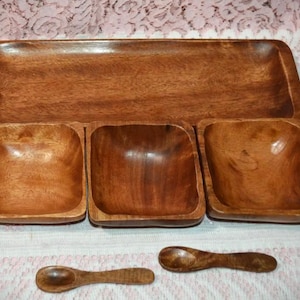 May include: A wooden serving set featuring a rectangular tray, three square bowls, and two small spoons. The set is made of a warm, medium-toned wood, showcasing the natural grain. Ideal for serving snacks or appetizers.