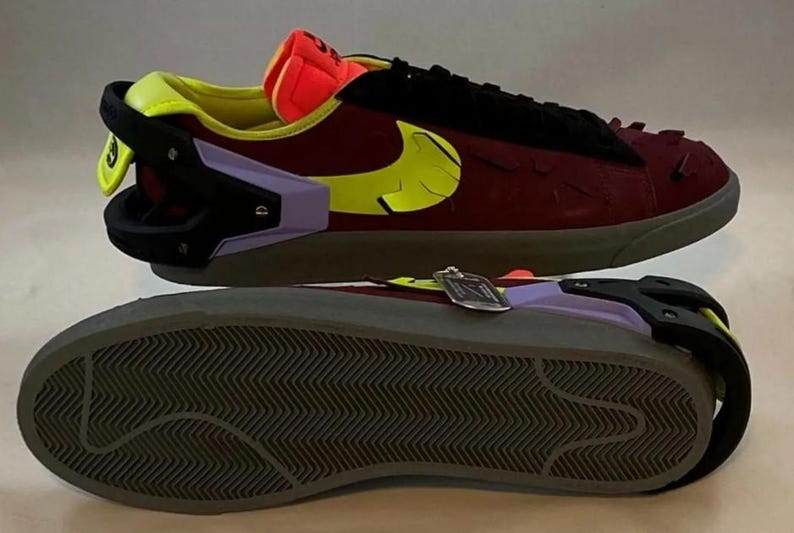 May include: Burgundy and black sneakers with a yellow Nike swoosh. The shoes have a unique design with a black heel counter, a purple accent, and a gray sole. The tongue is orange and yellow.