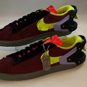 May include: A pair of burgundy sneakers with a neon yellow Nike swoosh and accents. The shoes have black laces, a gray sole, and a tag attached. The design includes a mix of textures and colors, creating a modern, athletic look.