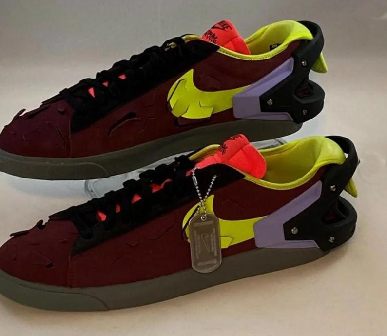 May include: A pair of burgundy sneakers with a neon yellow Nike swoosh and accents. The shoes have black laces, a gray sole, and a tag attached. The design includes a mix of textures and colors, creating a modern, athletic look.