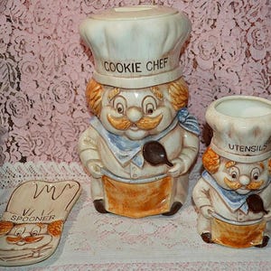 May include: A ceramic cookie jar, utensil holder, and spoon rest set. The cookie jar is shaped like a chef with the words "COOKIE CHEF" on the hat. The utensil holder is also a chef with the word "UTENSILS" on the hat. The spoon rest is shaped like a chef's hat with the word "SPOONER".