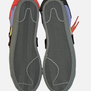 May include: Pair of colorful sneakers with gray soles. The shoes have a red, yellow, purple, and black color scheme. The soles have a textured, zigzag pattern. The shoes are shown from the bottom.