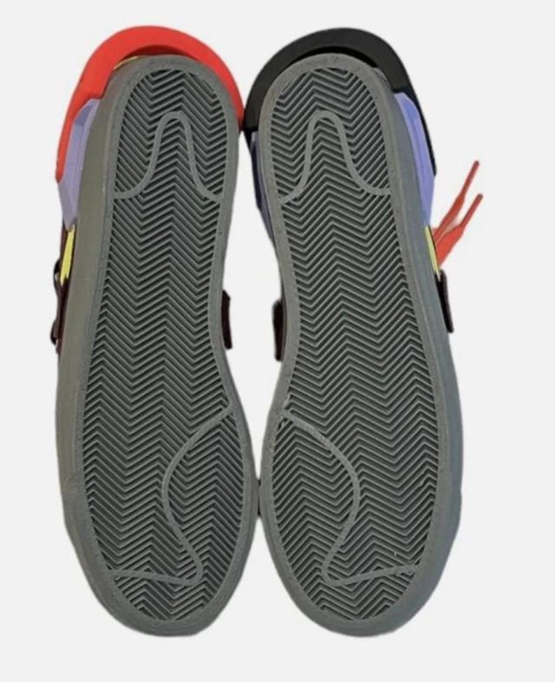 May include: Pair of colorful sneakers with gray soles. The shoes have a red, yellow, purple, and black color scheme. The soles have a textured, zigzag pattern. The shoes are shown from the bottom.