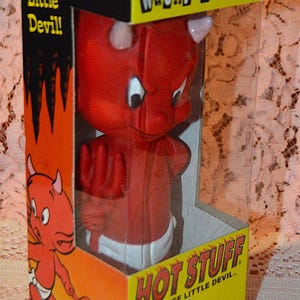 May include: A Hot Stuff Wacky Wobbler bobblehead figure inside its original yellow and orange cardboard box. The red devil character has small horns, a white diaper, and holds a red trident. The packaging features the text Hot Stuff The Tuff Little Devil.