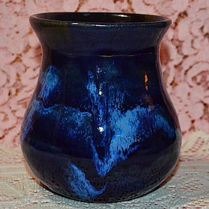 May include: A handcrafted ceramic vase with a glossy, dark blue glaze. The vase features a unique pattern of lighter blue streaks, creating a marbled effect. The vase has a rounded body and a slightly flared rim, suitable for displaying flowers.