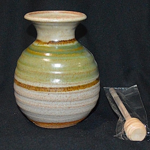 May include: A handcrafted ceramic vase with a wide base and a narrow neck, featuring horizontal bands of green, brown, and beige. A wooden honey dipper is included, packaged in a clear plastic bag. The vase is approximately 6 inches tall.