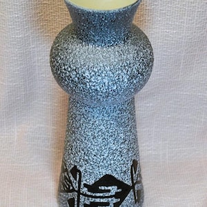 May include: A vintage ceramic vase with a speckled blue and white exterior. The vase has a bulbous midsection and a flared base. Black geometric designs adorn the lower portion. The interior is a pale yellow color.
