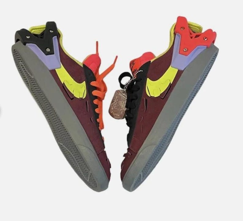 May include: Pair of high-top sneakers in a unique color block design. The shoes feature a burgundy base with yellow, orange, purple, and black accents. The soles are gray, and the laces are orange. A small tag hangs from one shoe.