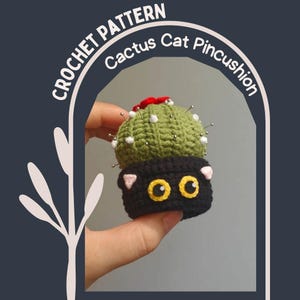 May include: A handmade crochet cactus cat pincushion. The cactus is green with white accents and red detailing, and the cat base is black with yellow eyes and pink ears. The text "CROCHET PATTERN Cactus Cat Pincushion" is in the image.