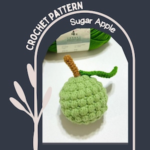May include: A crocheted sugar apple with a brown stem and green leaf. The apple is light green and has a textured surface. The image includes the text "CROCHET PATTERN" and "Sugar Apple".