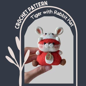 May include: A crocheted tiger doll wearing a white and red rabbit hat. The doll is red with brown feet and a gold-colored charm. The text "CROCHET PATTERN" and "Tiger with Rabbit Hat" are visible.