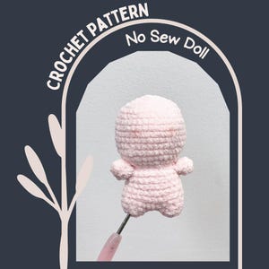 Puede incluir: Una muñeca de ganchillo rosa claro sostenida por un ganchillo. La muñeca tiene una cabeza y un cuerpo redondeados con brazos y piernas pequeños. La imagen incluye el texto "CROCHET PATTERN" y "No Sew Doll" en un arco blanco.