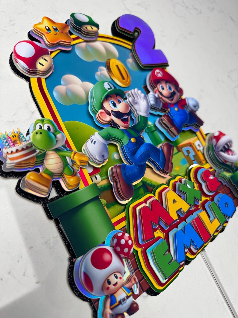 May include: A colorful cake topper featuring characters from the Super Mario Bros. video game. The design includes Mario, Luigi, Yoshi, and Toad, with a number 2 and the names "Max & Emilio". The background depicts a blue sky with clouds.