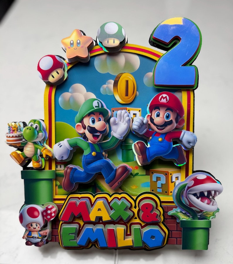 May include: A colorful cake topper featuring Mario and Luigi characters, a green Yoshi, and a Piranha Plant. The design includes a blue number 2, a gold coin, and the names "MAX & EMILIO". The background is a blue sky with clouds.