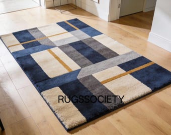 May include: Rectangular rug featuring a geometric design in navy blue, beige, grey, and gold. The rug is placed on a wooden floor. The text "RUGSSOCIETY" is visible on the rug.