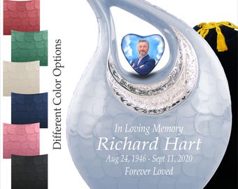 May include: A light blue memorial urn with a heart-shaped photo frame. The urn has a textured surface and silver accents. Text reads "In Loving Memory Richard Hart Aug 24, 1946 - Sept 11, 2020 Forever Loved". Different color options are shown.
