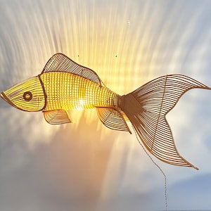 Könnte beinhalten: Dekorative Fisch-förmige Leuchte aus geflochtenem Bambus. Die Leuchte wird von innen beleuchtet und erzeugt einen warmen Schein. Der Fisch hat einen detaillierten Schwanz und Flossen und hängt von der Decke.