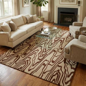 May include: A living room scene with a beige sofa, armchairs, and a glass coffee table. A large rug with a beige base and a brown, flowing, organic pattern dominates. The room has wooden flooring and a fireplace. The rug's pattern resembles tree rings.