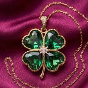 May include: A gold-toned necklace featuring a four-leaf clover pendant with four large, faceted, deep green crystals. The centre of the clover is accented with a small cluster of clear, sparkling stones, and the pendant hangs from a delicate gold chain.