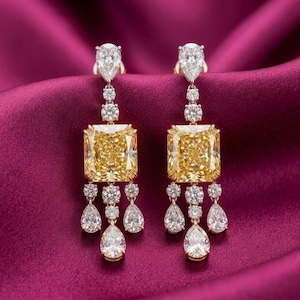 May include: A pair of drop earrings featuring a large square-cut yellow gemstone at the center, topped with a pear-cut white stone and accented by multiple smaller round white stones and three dangling pear-cut white stones at the base.