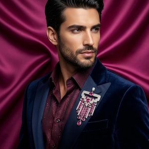 May include: A navy blue velvet blazer with a burgundy shirt, adorned with a sparkling brooch. The brooch features a rectangular design with white and pink gemstones, and dangling pink teardrop gems. The background is a deep magenta.