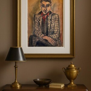 Op de afbeelding: Een ingelijst olieverfschilderij van een zittende figuur in een geruit jasje en een rood overhemd hangt boven een donkere houten tafel. Een messing lamp, een kom, een boek en een decoratieve urne staan op de tafel. De muur is geschilderd in een warme bruine kleur.