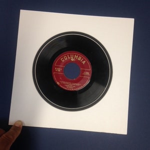 May include: A black vinyl record with a white label that says "Columbia 45" in red lettering. The record is in a white mat.