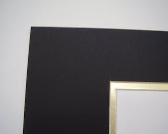 May include: Black mat board with a gold border around the opening. The mat board is used for framing artwork or photos.