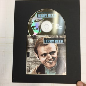 May include: A black framed CD with a picture of Jerry Reed on the cover. The title of the CD is "The Essential Jerry Reed".