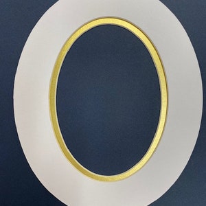 May include: A white oval picture frame with a gold inner border. The frame is set against a dark blue background, creating a contrast that highlights the frame's shape and design. The frame is a decorative item.