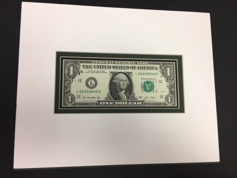 May include: A framed one dollar bill with a green border. The bill features a portrait of George Washington and the text "THE UNITED STATES OF AMERICA" and "ONE DOLLAR".