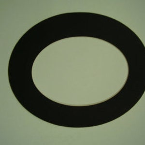 K&ouml;nnte beinhalten: Ein schwarzes, oval geformtes Objekt mit einem helleren, ovalen Zentrum. Das Objekt scheint ein flaches, ringf&ouml;rmiges Element zu sein, m&ouml;glicherweise eine Dichtung oder ein dekoratives Element. Der Hintergrund ist einfarbig hellgr&uuml;n.