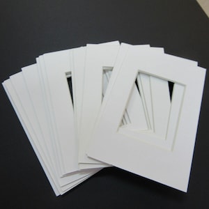 May include: A stack of white mat boards with a square opening in the center. The mat boards are used for framing artwork or photographs.