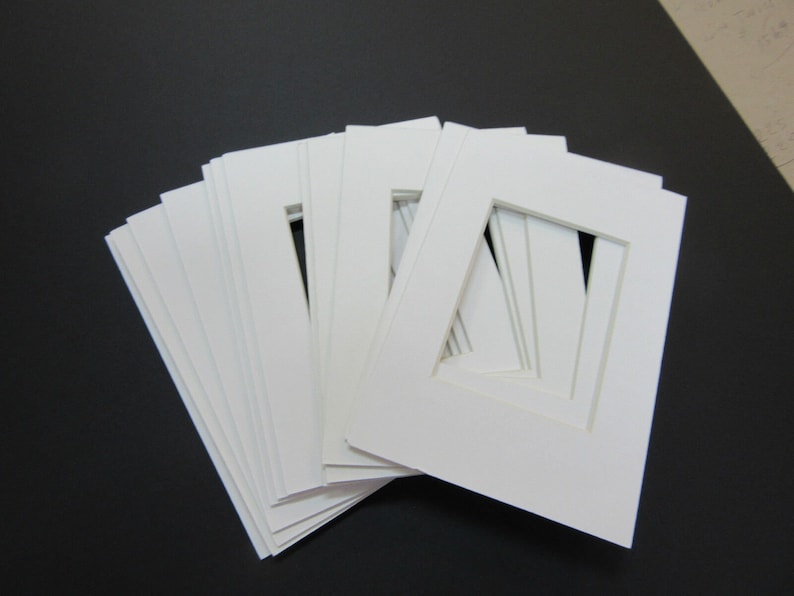 May include: A stack of white mat boards with a square opening in the center. The mat boards are used for framing artwork or photographs.