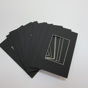 May include: A stack of black mat boards with white cut-out openings. The mat boards are arranged in a fan shape.
