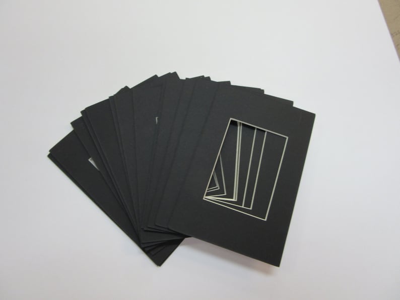 May include: A stack of black mat boards with white cut-out openings. The mat boards are arranged in a fan shape.