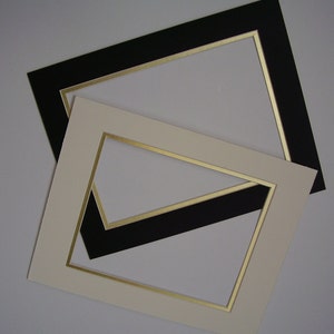 May include: Two picture frames with gold trim. The top frame is black and the bottom frame is cream.