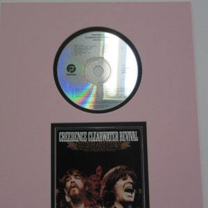 May include: A black and white CD case with a photo of the band Creedence Clearwater Revival. The text on the case reads "Creedence Clearwater Revival - Green River -  The 20th Anniversary Collection".