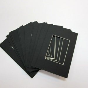 May include: A stack of black mat boards with a white window opening. The mat boards are used for framing artwork or photos.