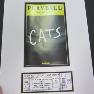 May include: A framed Playbill from the Neil Simon Theatre for the musical "Cats", with a matching ticket stub. The Playbill features the show's title in large white letters against a dark background.