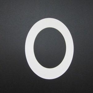 K&ouml;nnte beinhalten: Ein wei&szlig;er, oval geformter Papierauschnitt vor einem schwarzen Hintergrund. Der Ausschnitt hat einen dicken Rand und eine hohle Mitte, die dem Buchstaben "O" &auml;hnelt. Das Bild ist ein einfaches, kontrastreiches Design.