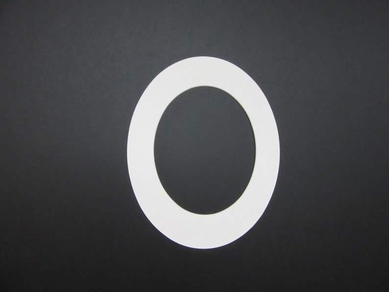 K&ouml;nnte beinhalten: Ein wei&szlig;er, oval geformter Papierauschnitt vor einem schwarzen Hintergrund. Der Ausschnitt hat einen dicken Rand und eine hohle Mitte, die dem Buchstaben "O" &auml;hnelt. Das Bild ist ein einfaches, kontrastreiches Design.