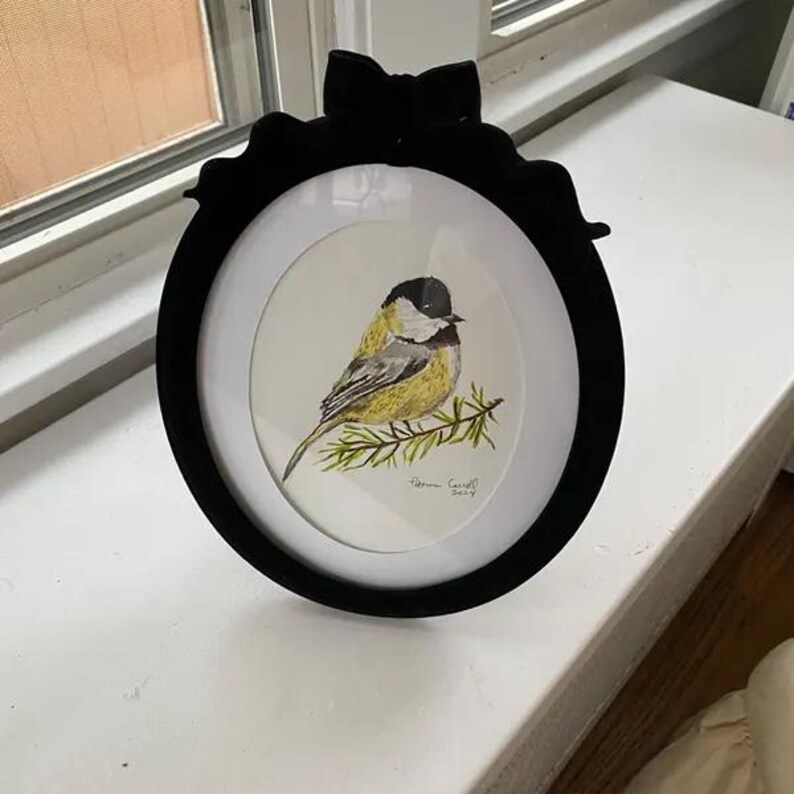 K&ouml;nnte beinhalten: Ein gerahmtes Aquarellgem&auml;lde einer Kohlmeise, die auf einem Ast sitzt. Der Vogel hat einen schwarzen Kopf, einen gelben K&ouml;rper und graue Fl&uuml;gel. Das Gem&auml;lde befindet sich in einem runden Rahmen mit einer schwarzen Schleife oben. Der Rahmen hat einen Durchmesser von etwa 20 cm.