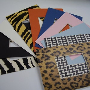 May include: Assortment of colorful and patterned mat boards with cut-out windows for framing photos or artwork. The mat boards feature a variety of designs, including animal prints, geometric patterns, and solid colors.