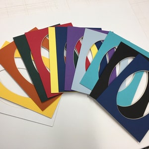 May include: A set of 10 oval-shaped mat boards in various colors, including yellow, red, green, blue, purple, and black. The mat boards are arranged in a fan shape, with the largest board at the bottom and the smallest board at the top.