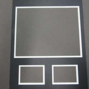 May include: A black mat with a white border, featuring a large rectangular opening and two smaller rectangular openings below it. The mat is designed for displaying photos or artwork.