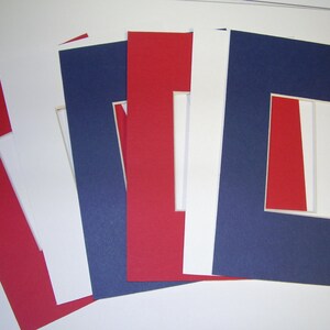 Puede incluir: Cinco cartulinas de colores diferentes con una abertura blanca en el centro. Las cartulinas son rojas, blancas, azules y dos tonos de rojo.